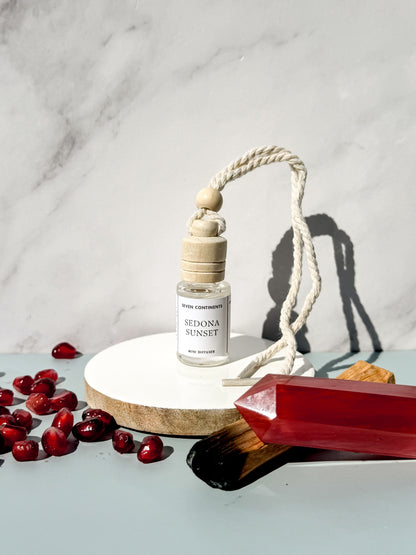 Sedona Sunset car diffuser with wooden cap on a white marble surface with red berries and a red crystal.